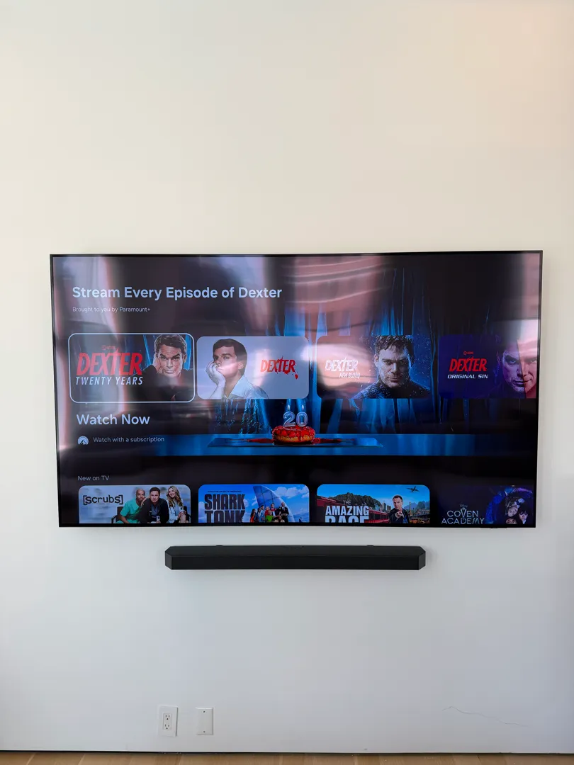 The same large TV and soundbar on the clean white wall, viewed straight on.