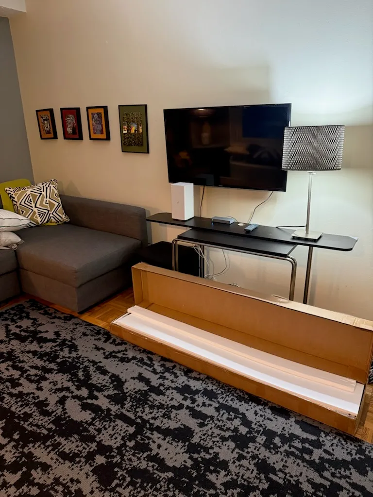 A TV already mounted above a narrow table, with a large unopened console box on the floor in front.