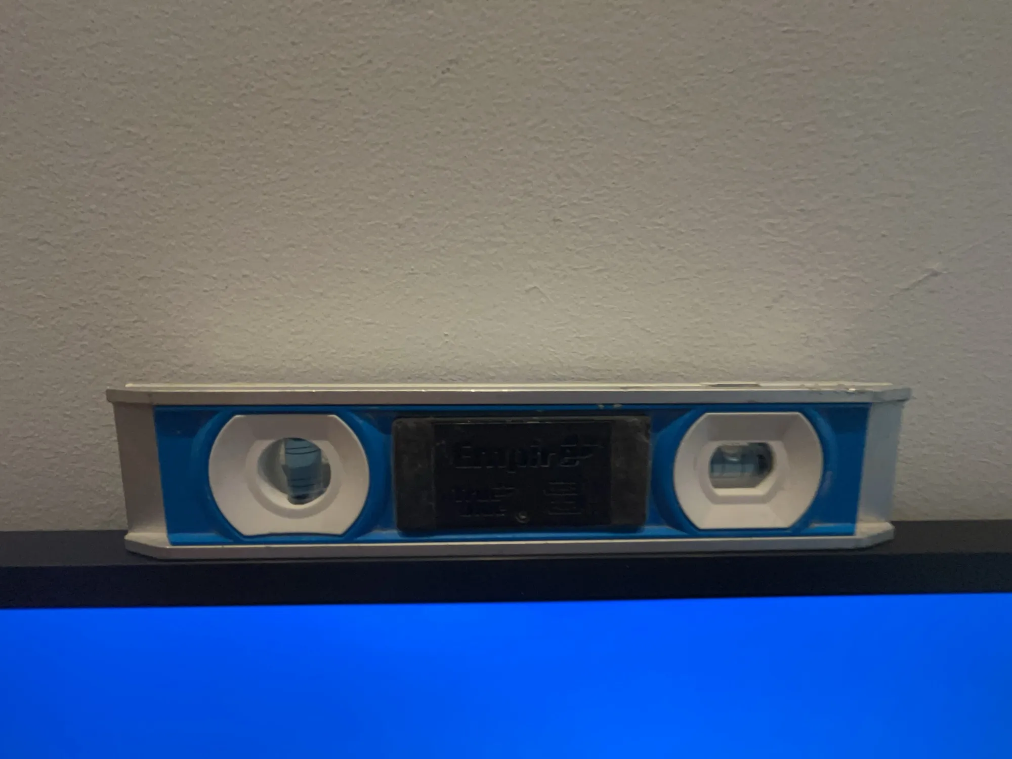 A blue level tool on top of a TV screen checking the mount.