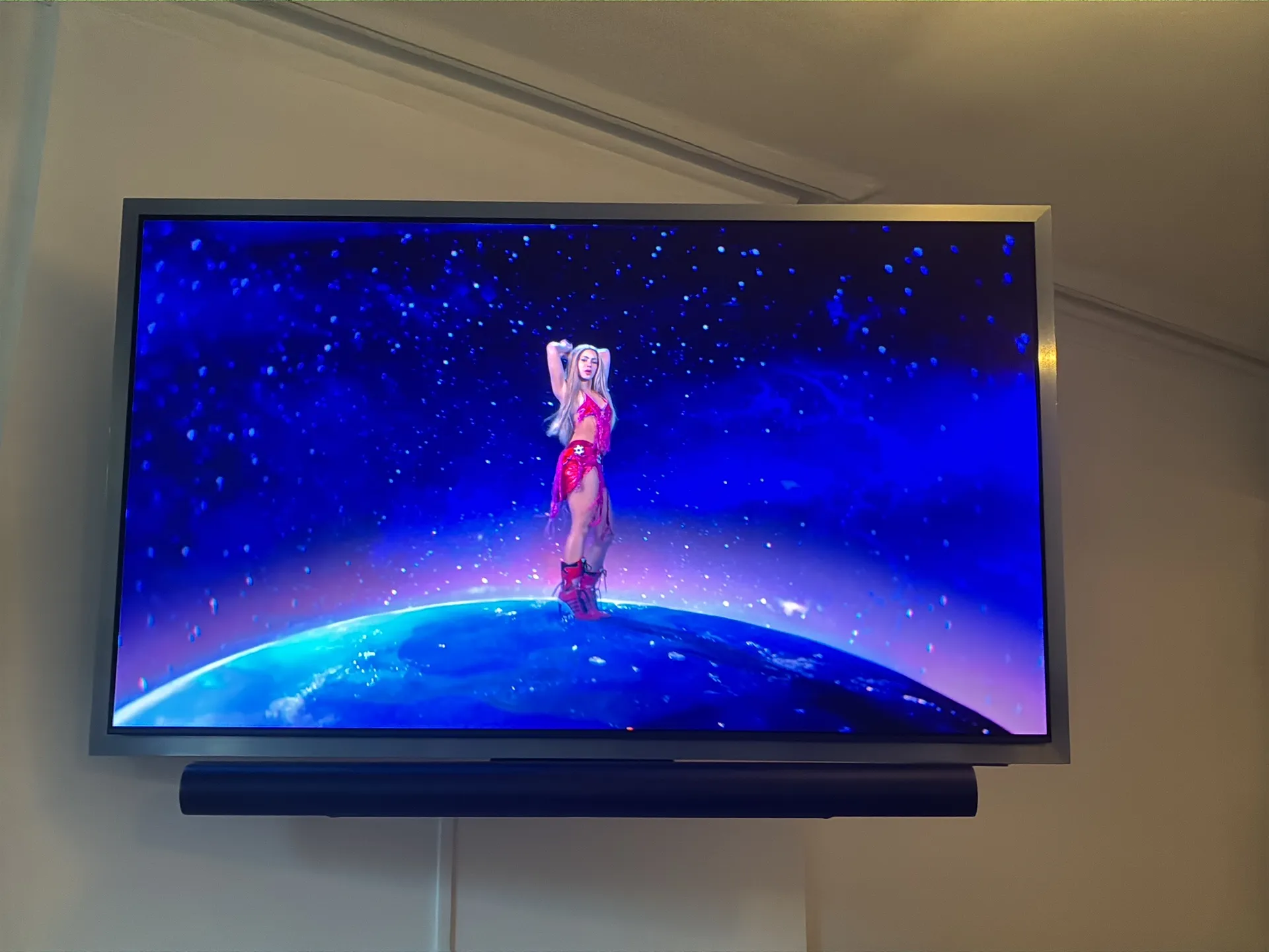 A close view of a wall-mounted TV with a soundbar below it and a white cable running down the wall.