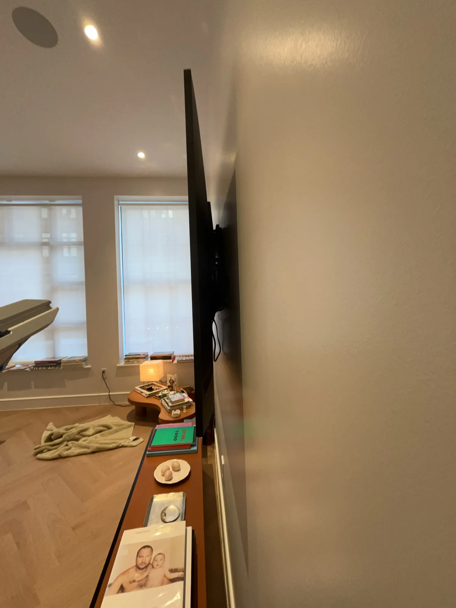 A wall-mounted flat-screen TV seen from a corner, with windows and a media console below.