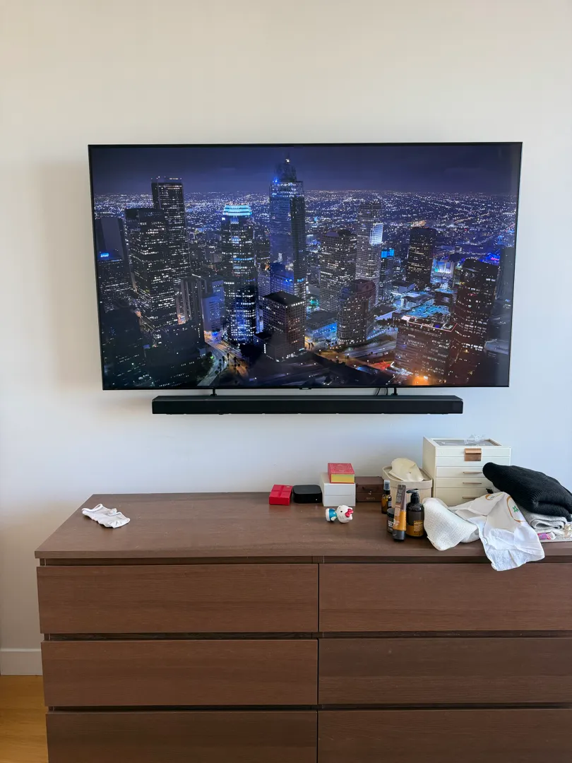 A wall-mounted TV with a soundbar below it above a wooden dresser, with no cords showing.