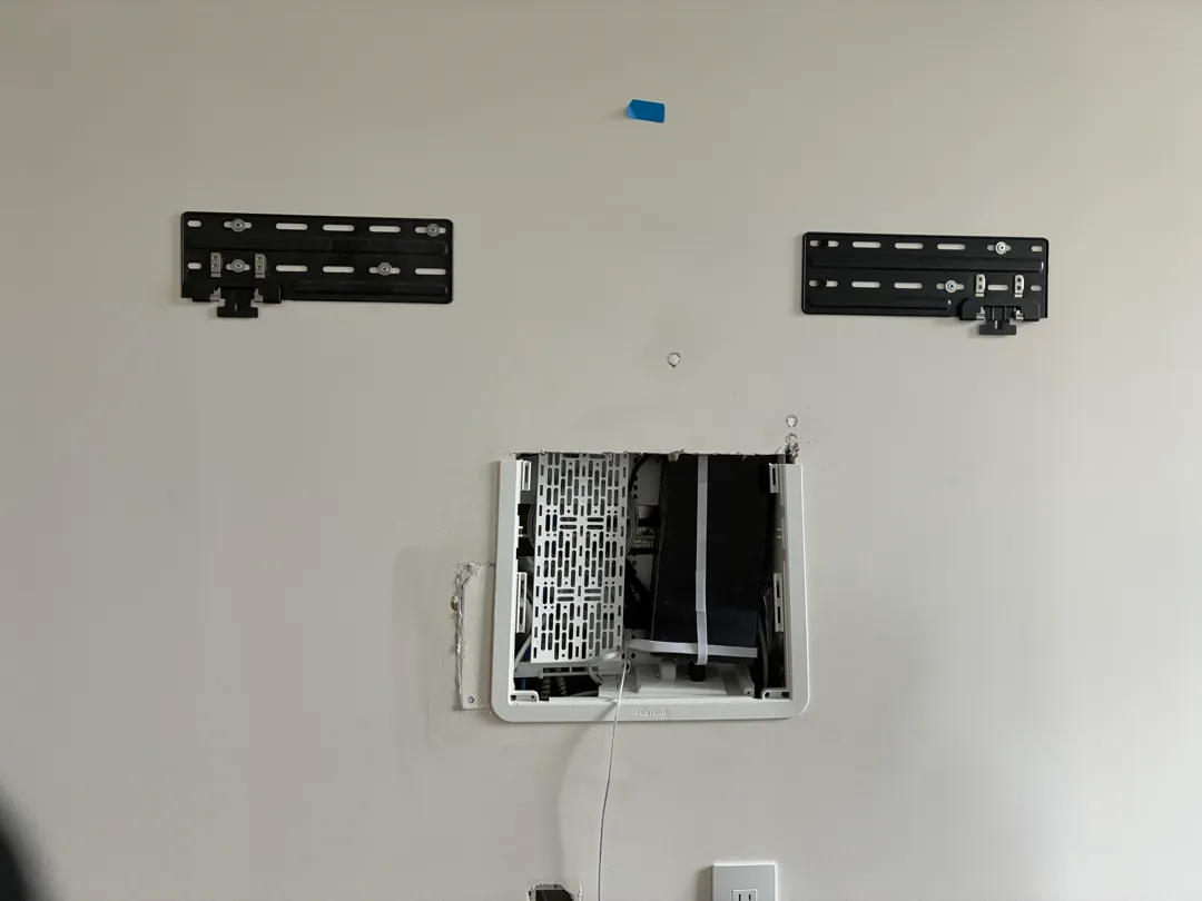 Two black TV mount brackets fixed to a wall above a white recessed box.