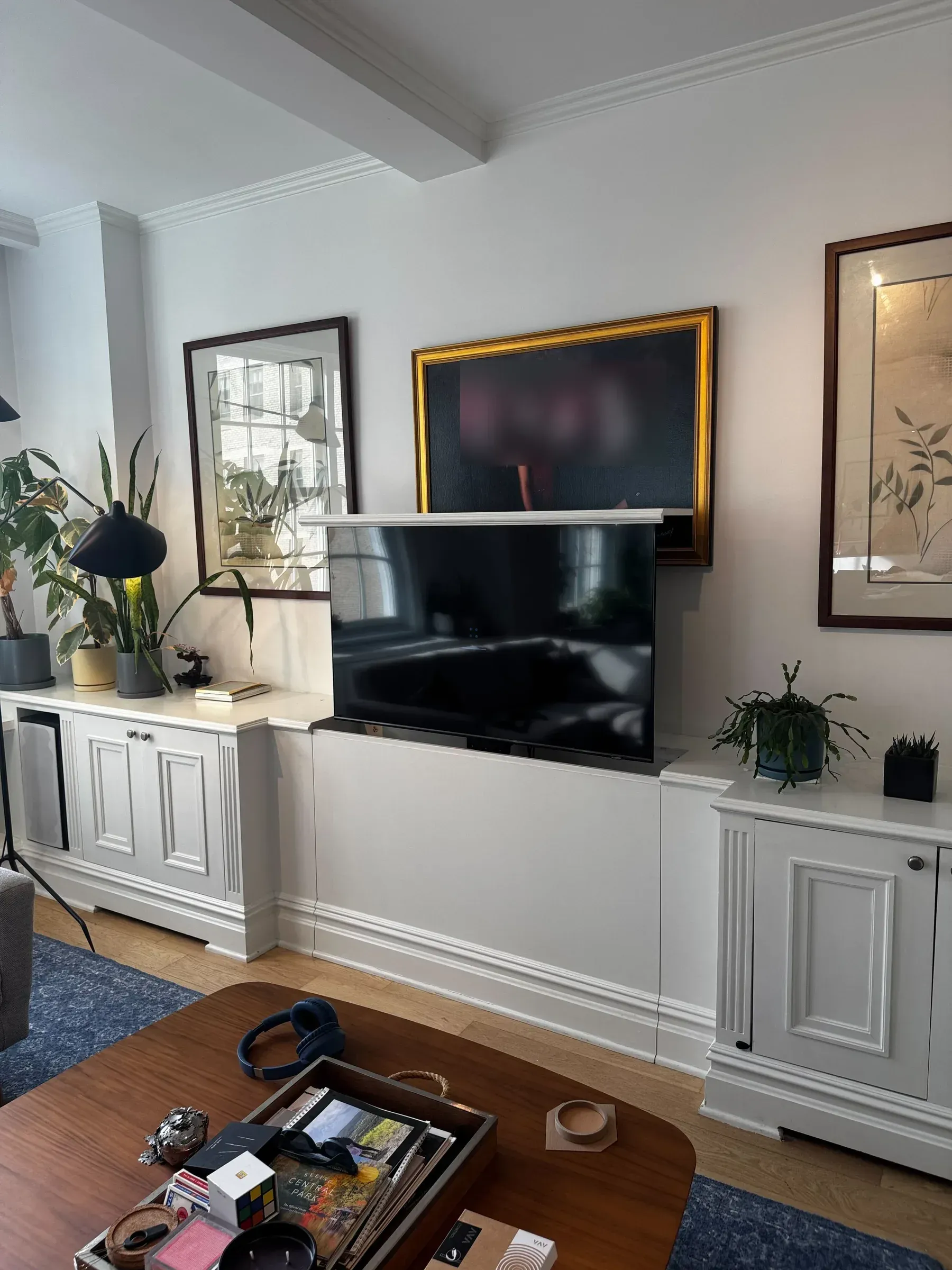 A TV rises from a motorized lift built into a white cabinet below a framed family portrait.