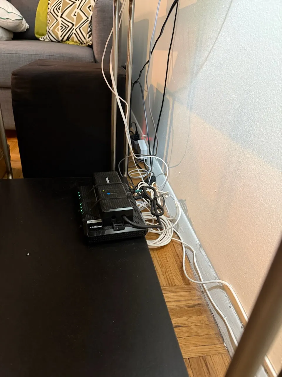 A router on a table edge with a tangle of cables running down to the baseboard.