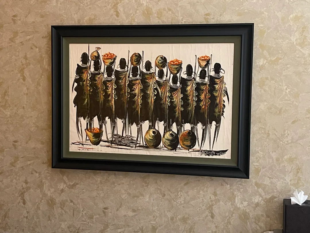 A large black-framed painting of standing figures hanging on a textured gold-toned wall.