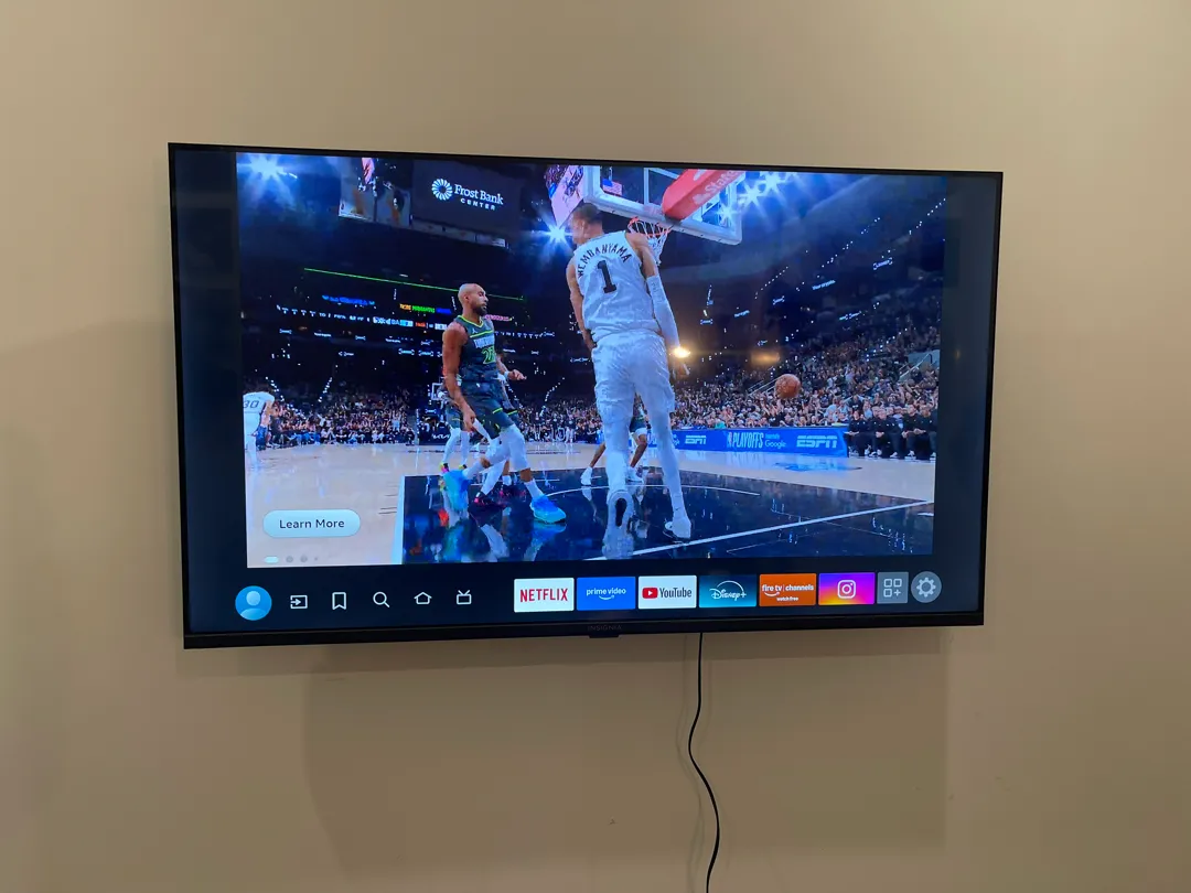 A flat TV hangs on a beige wall playing a basketball game.