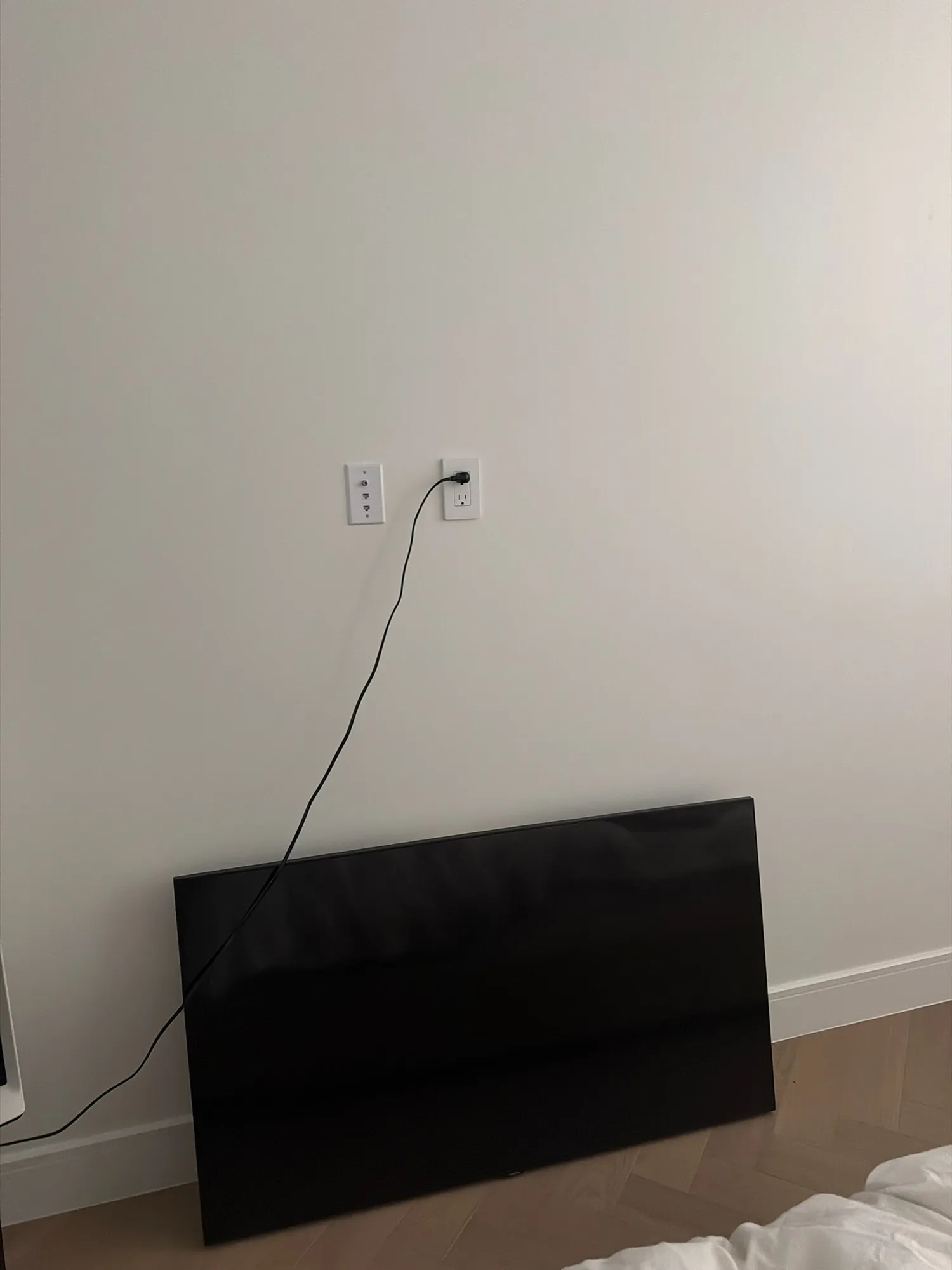 An unmounted flat-screen TV leaning against a bedroom wall, with a cord running up to an outlet.