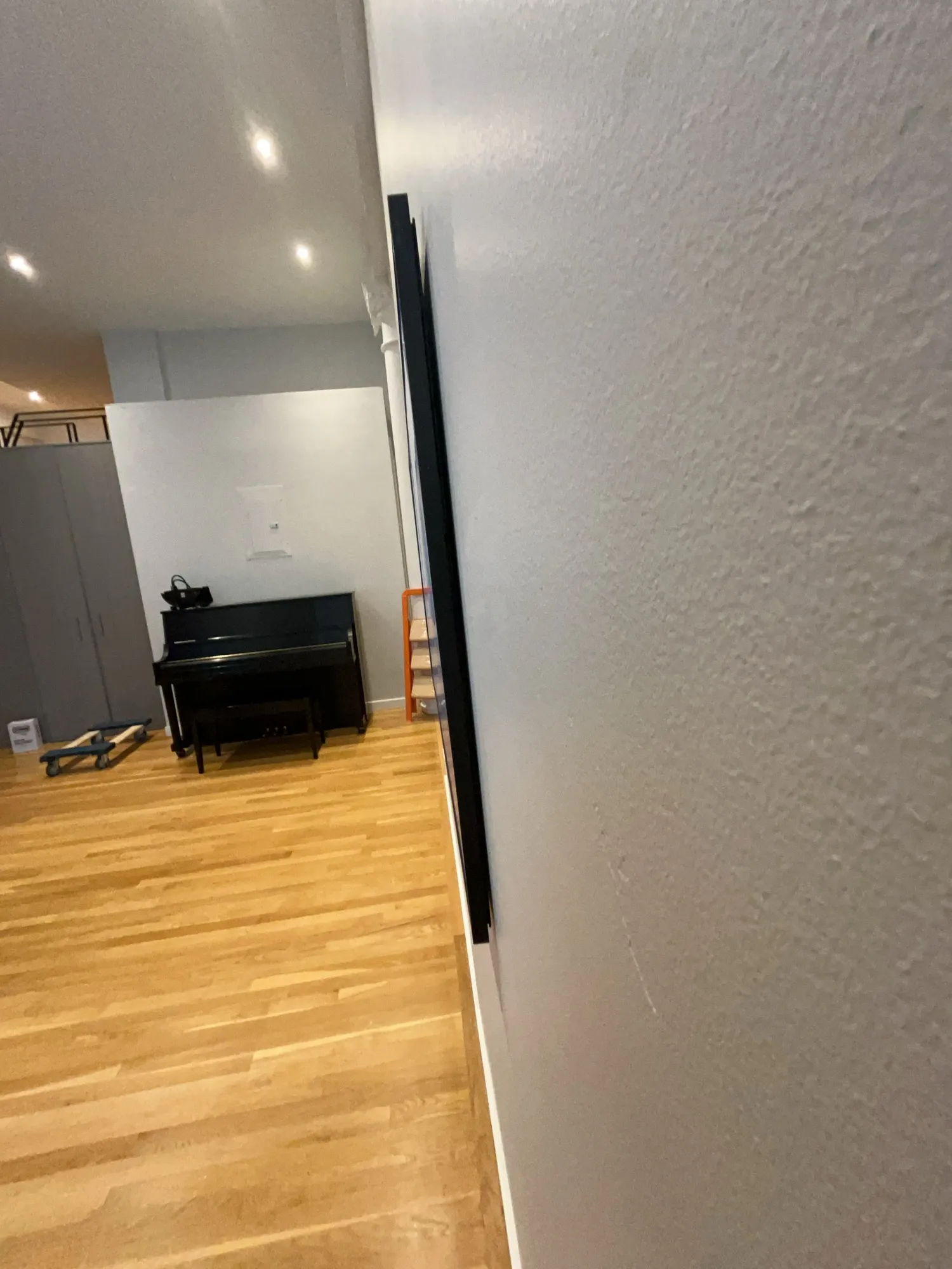 An open room with a piano, a furniture dolly, and a leaning panel.