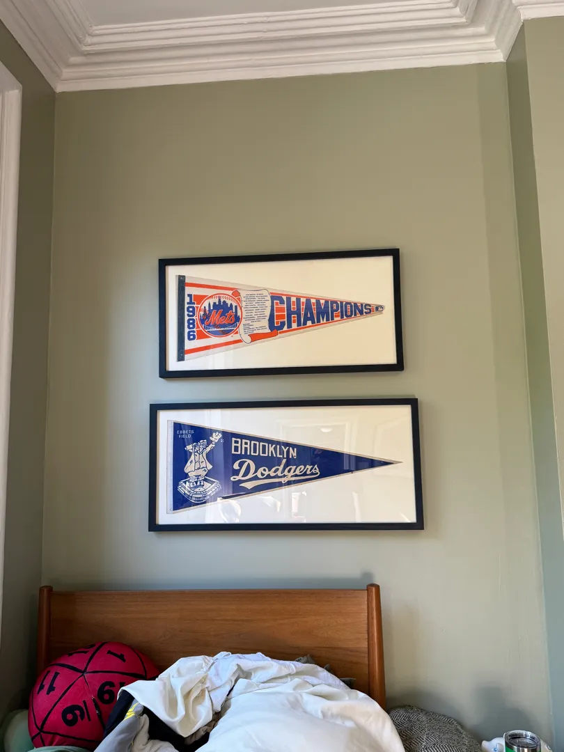 Two framed vintage sports pennants mounted above a wood headboard.