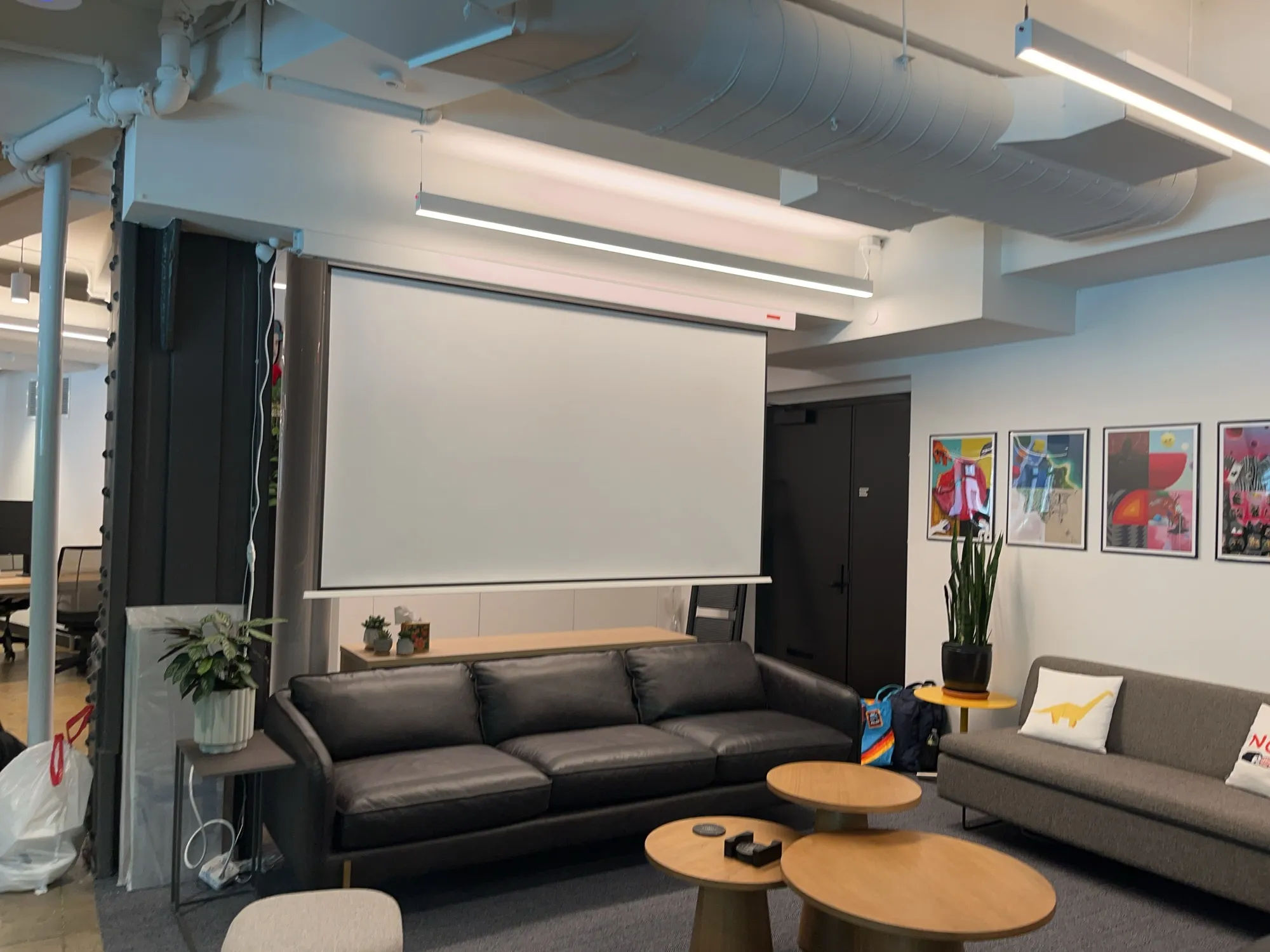 A pull-down projector screen lowered above a leather sofa in an office lounge.