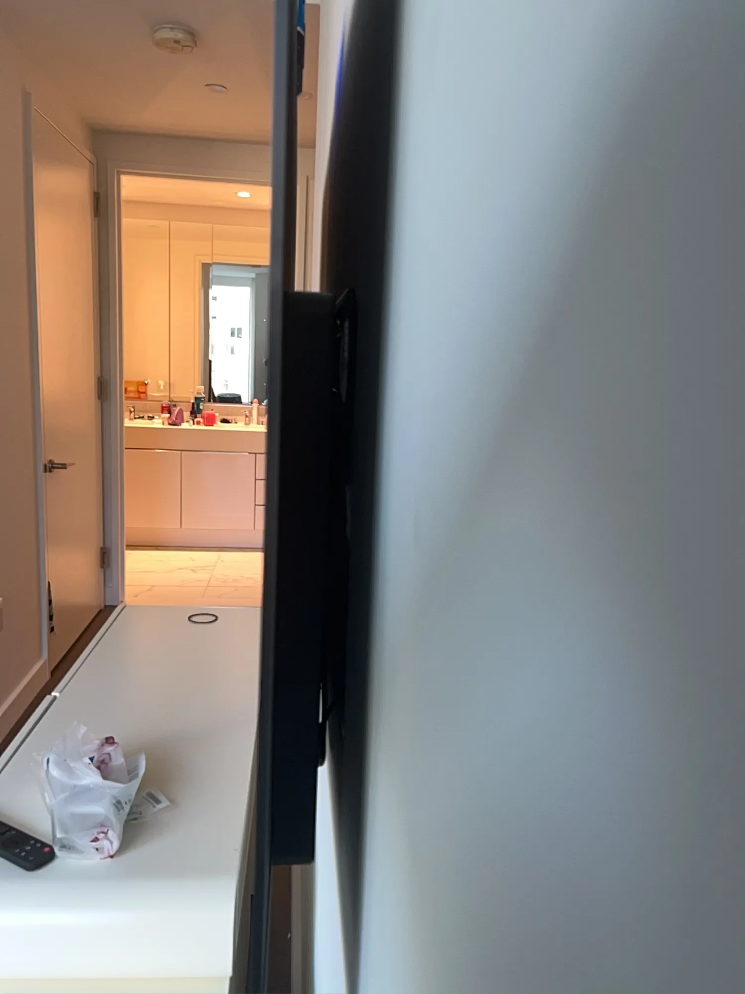 The edge of a newly mounted TV, seen from the side, looking down a hallway into a bathroom.