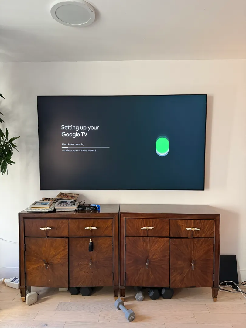 The mounted TV continues its Google TV setup, showing further install progress above the credenza.