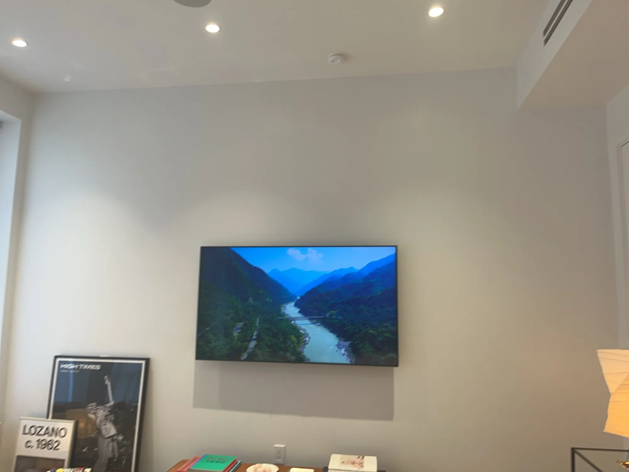 A flat-screen TV mounted on a living room wall above a console with books and a framed poster.