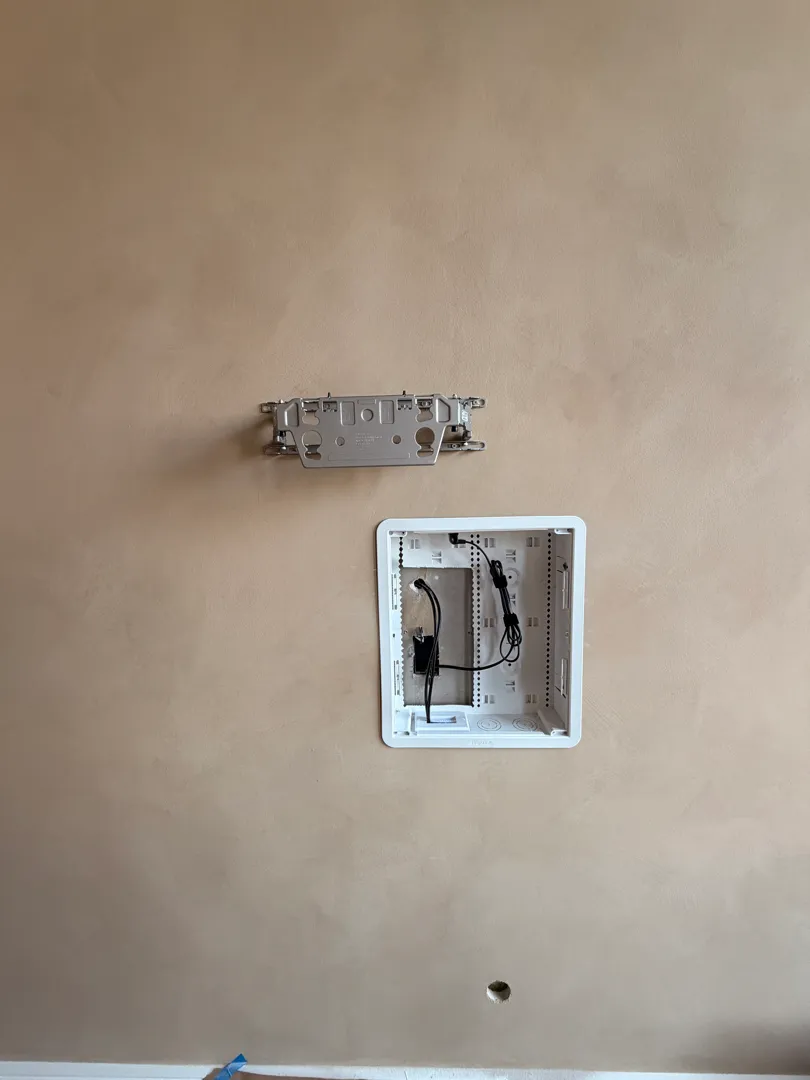 A mounting bracket plate and an open in-wall cable box with wires are installed on the wall, no TV yet.