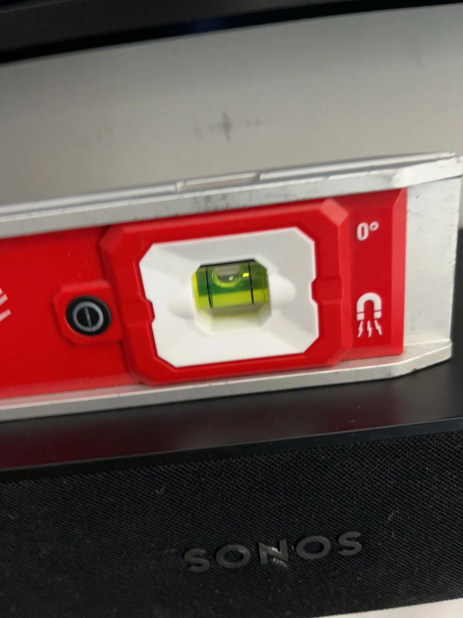 A red level tool held against the bottom edge of a TV, with a soundbar visible below it.