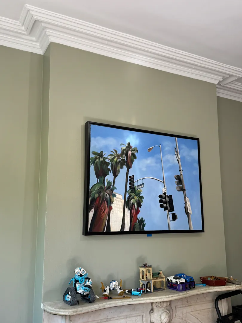 A framed painting of palm trees and traffic signals, mounted above a marble mantel.