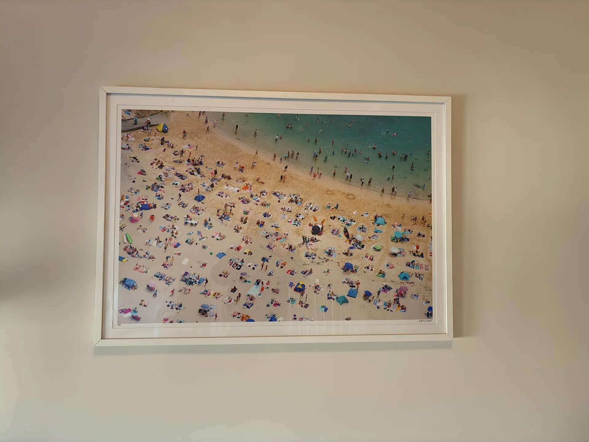 A large white-framed aerial beach photograph hanging on a cream wall.
