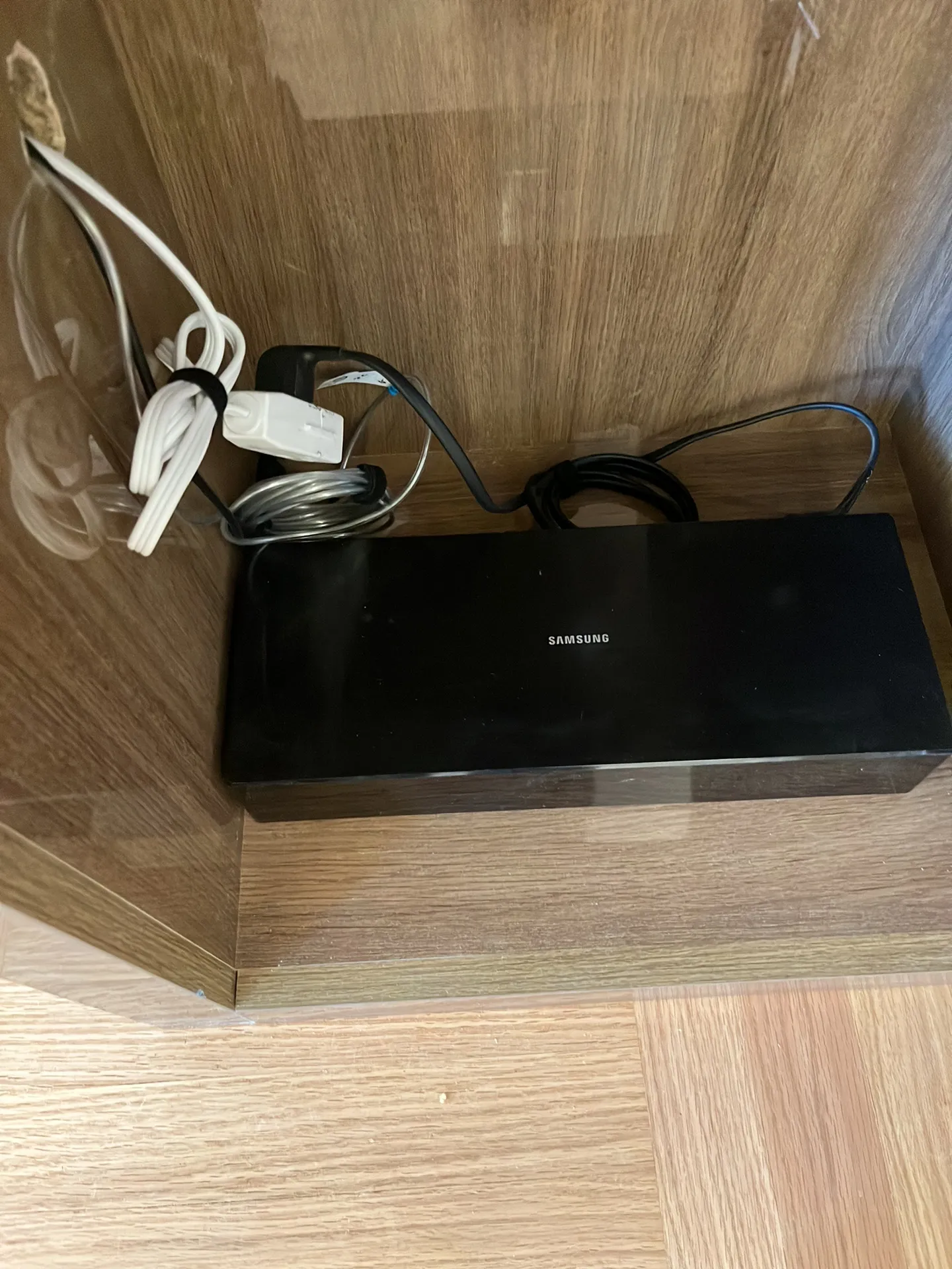 A black Samsung media box sits in a wood cabinet corner with cables bundled and routed neatly beside it.