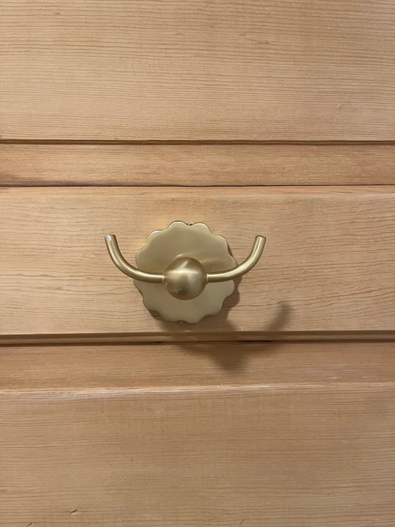 A gold double-hook mounted on a wood-paneled cabinet.