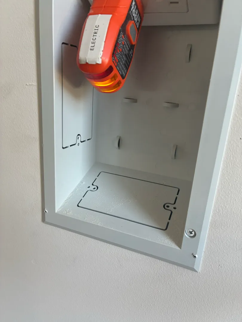 An orange power screwdriver is used inside an open in-wall box during installation.