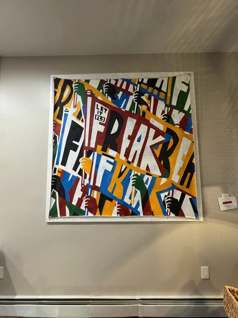 A large, colorful canvas art piece with bold graphic lettering, hung on a plain wall.