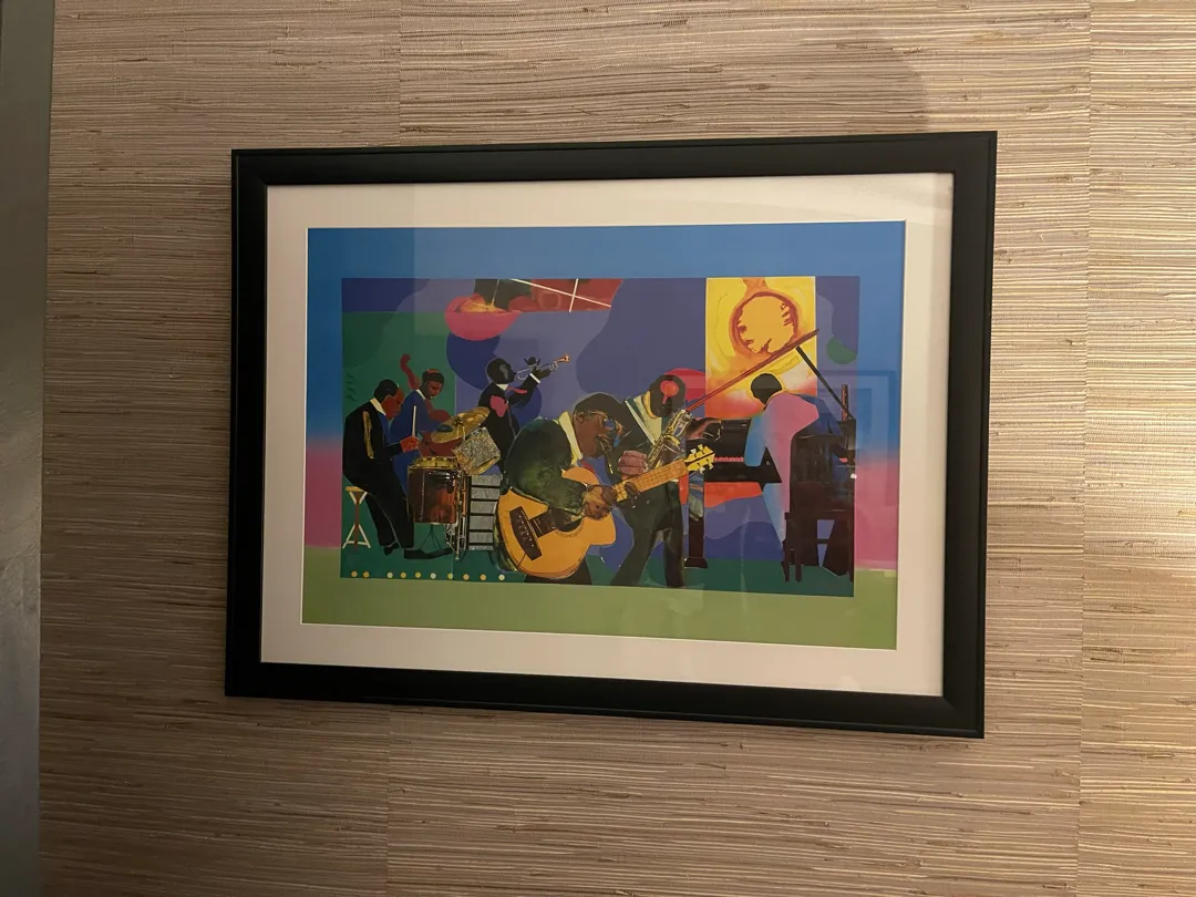A black-framed colourful jazz print with a white mat hanging on a grasscloth wall.