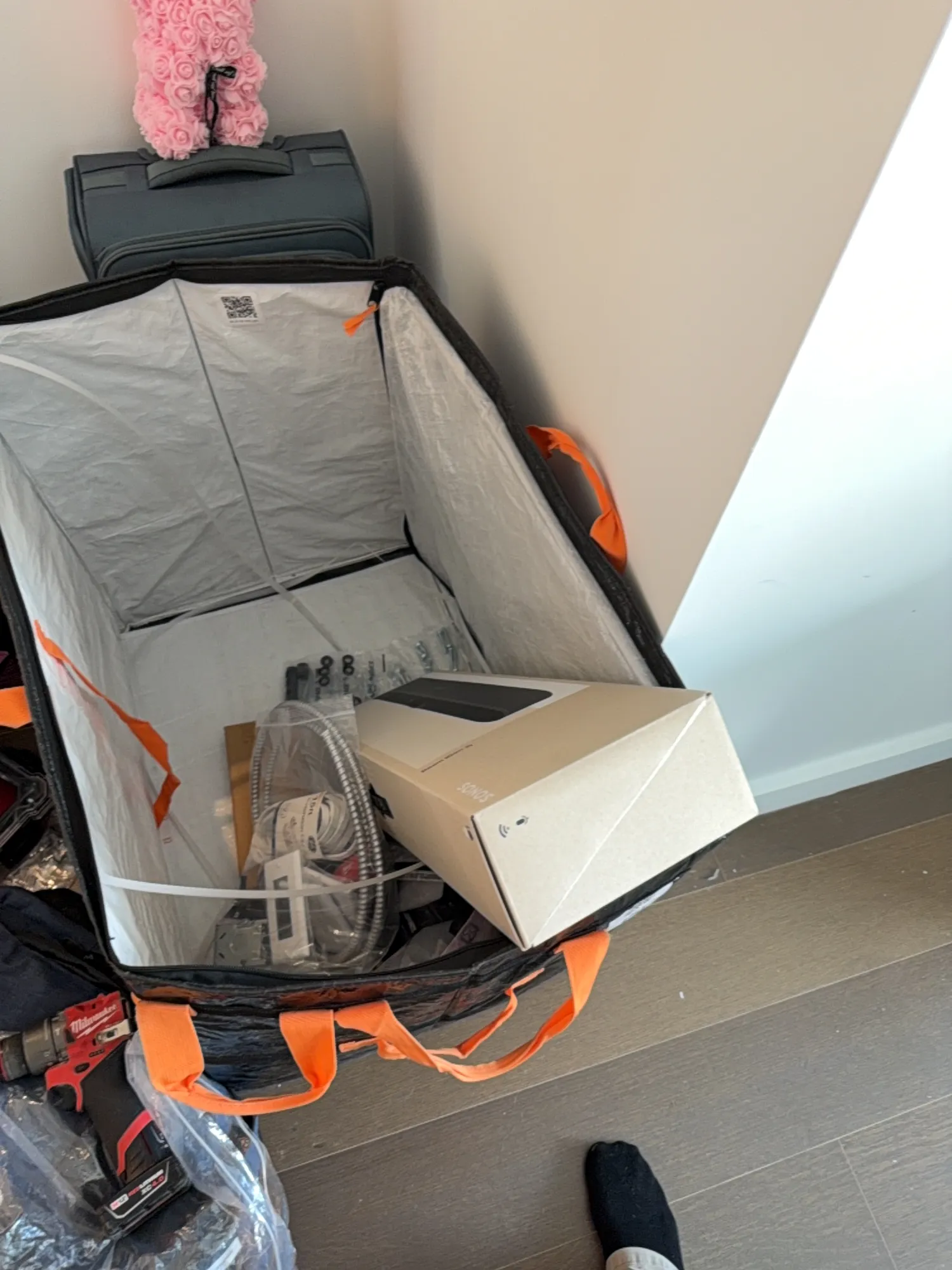 An open equipment case on the floor, holding tools, cable, an outlet box kit, and a boxed Sonos product.