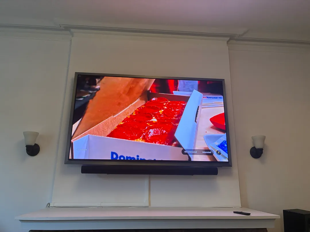 A TV with a soundbar below it above a fireplace mantel between two wall lights.