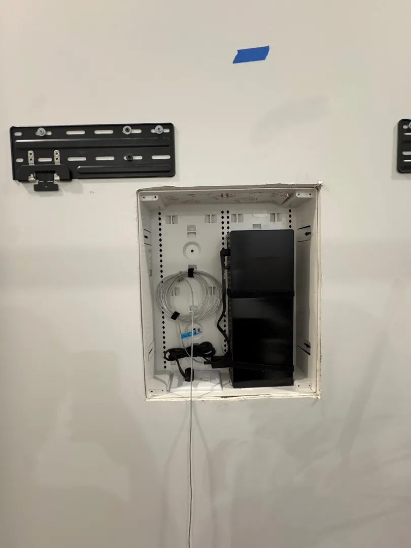 Open recessed AV box holding a device and cables below Frame TV mount plates.