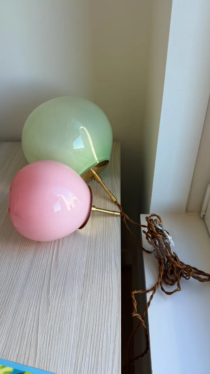 Two glass globe pendants on a cabinet with a gold stem and a coiled brown fabric cord.