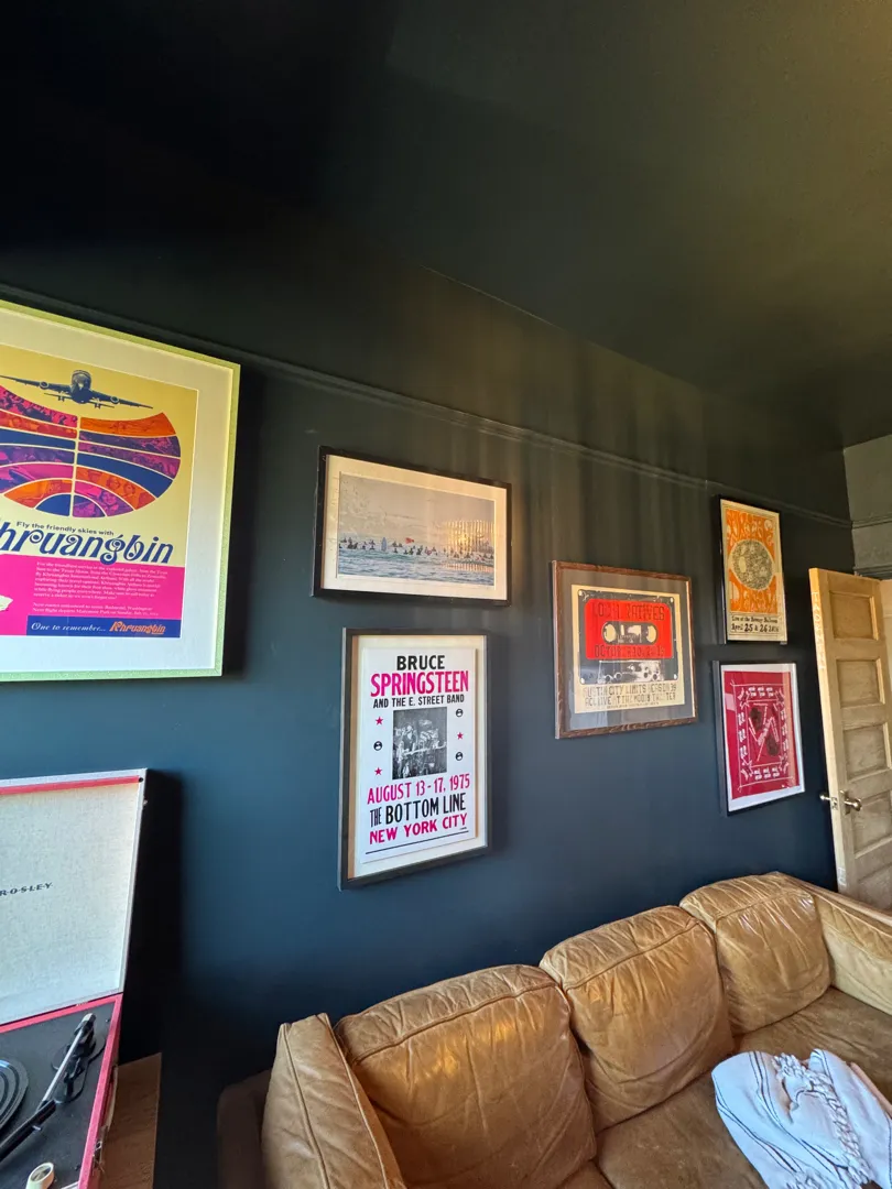 A dark lounge with a gallery wall of framed concert posters above a leather sofa.