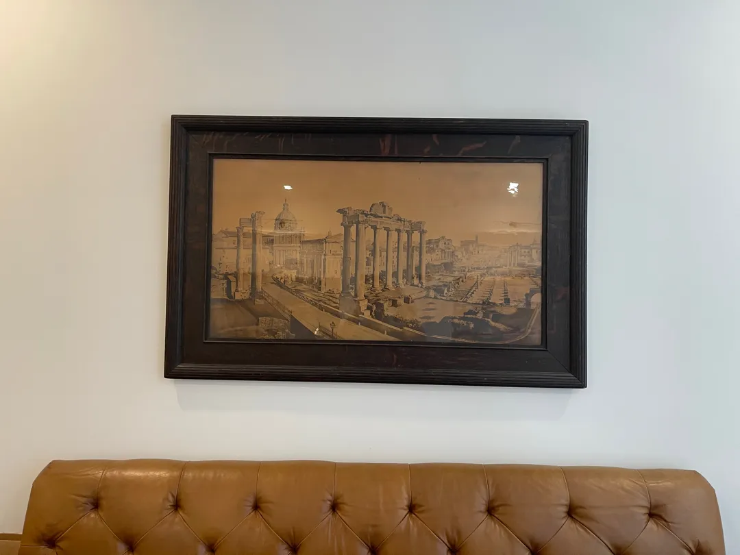 Large dark-framed architectural picture mounted above a tan leather sofa.