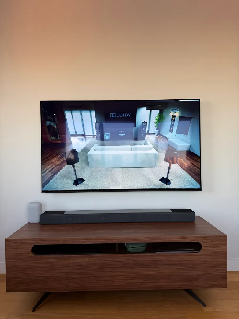 A thin wall-mounted TV sitting flush above a walnut media console with a soundbar and a small speaker, with no cords showing.