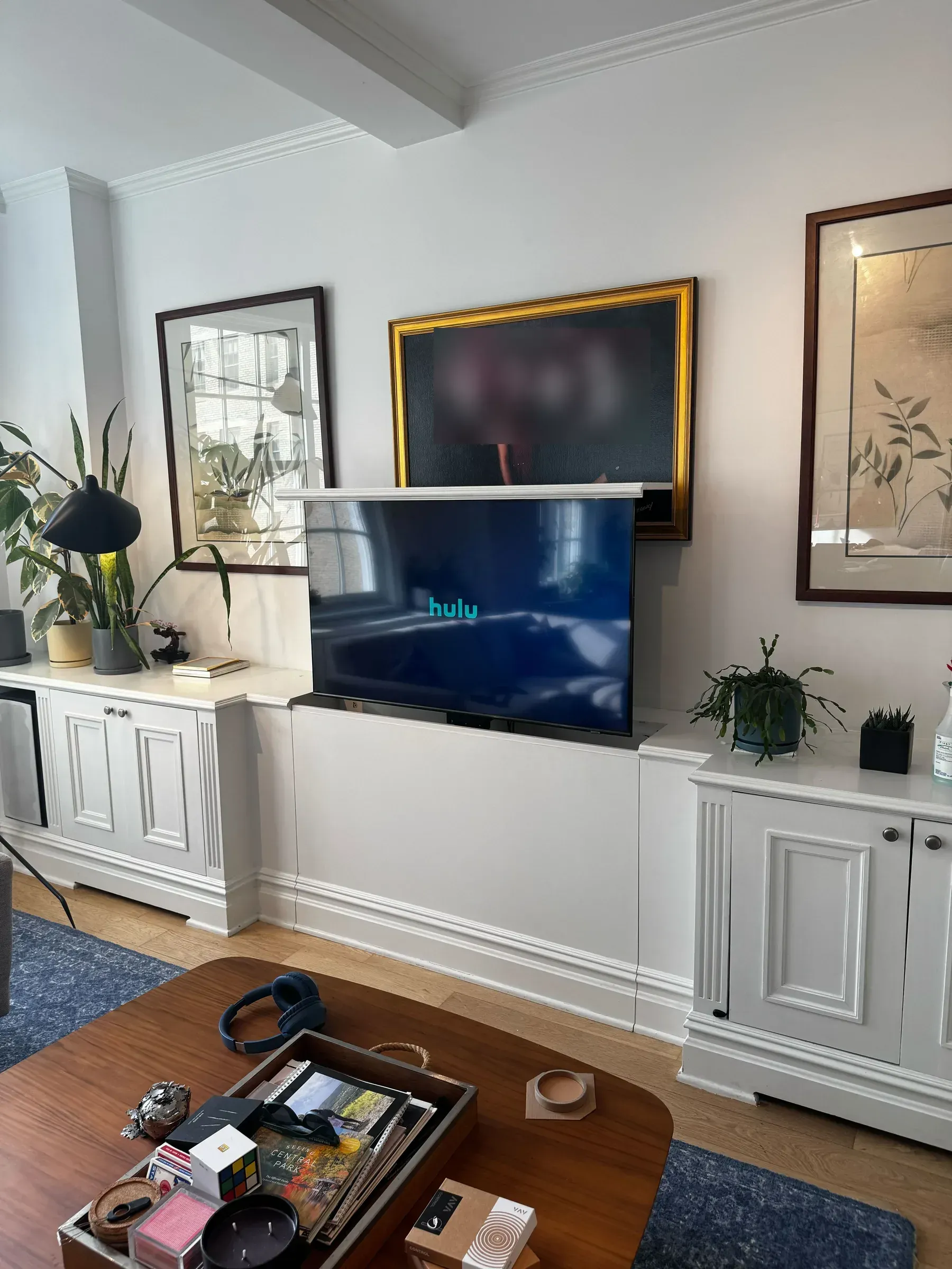 A TV raised above a white cabinet, playing a streaming app, below a framed family portrait.