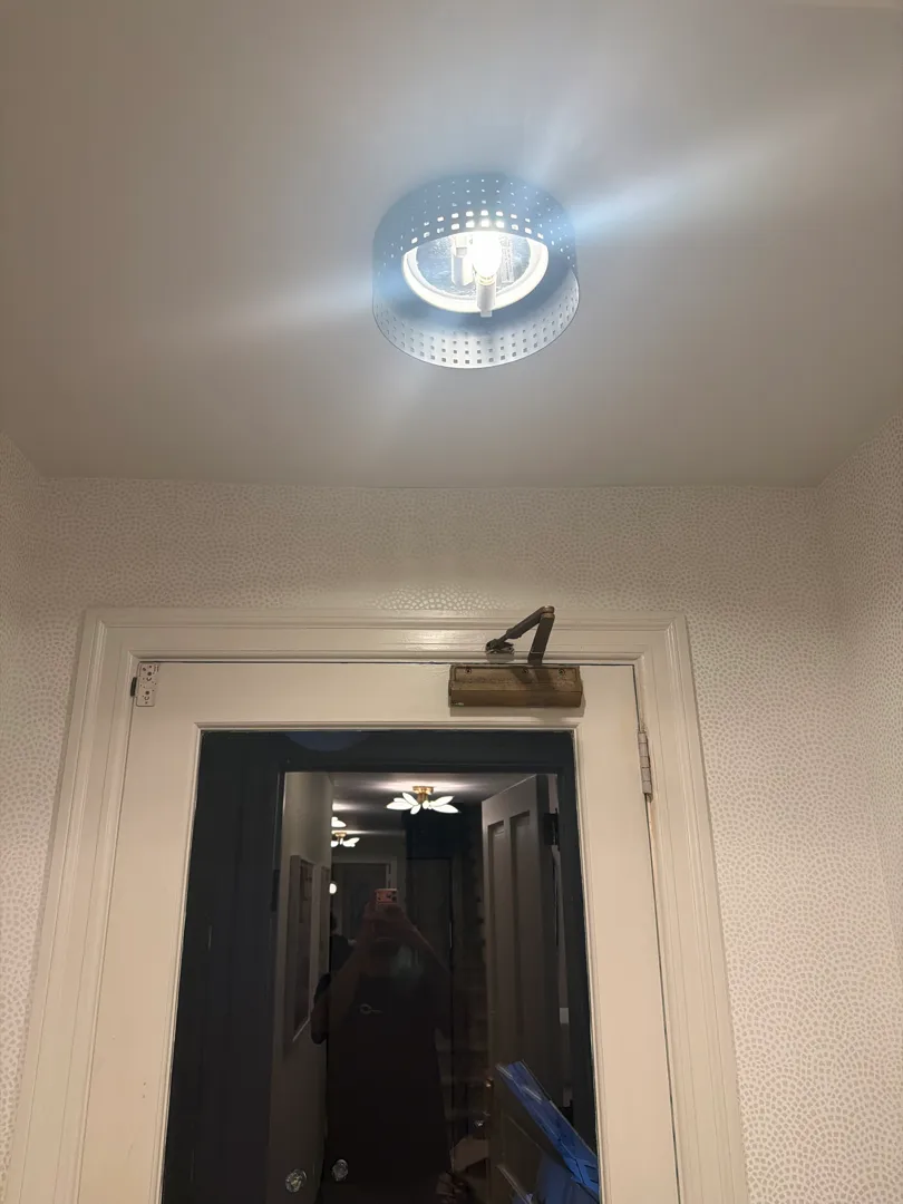 A round ceiling light fixture is installed and turned on above a doorway leading to a hallway.