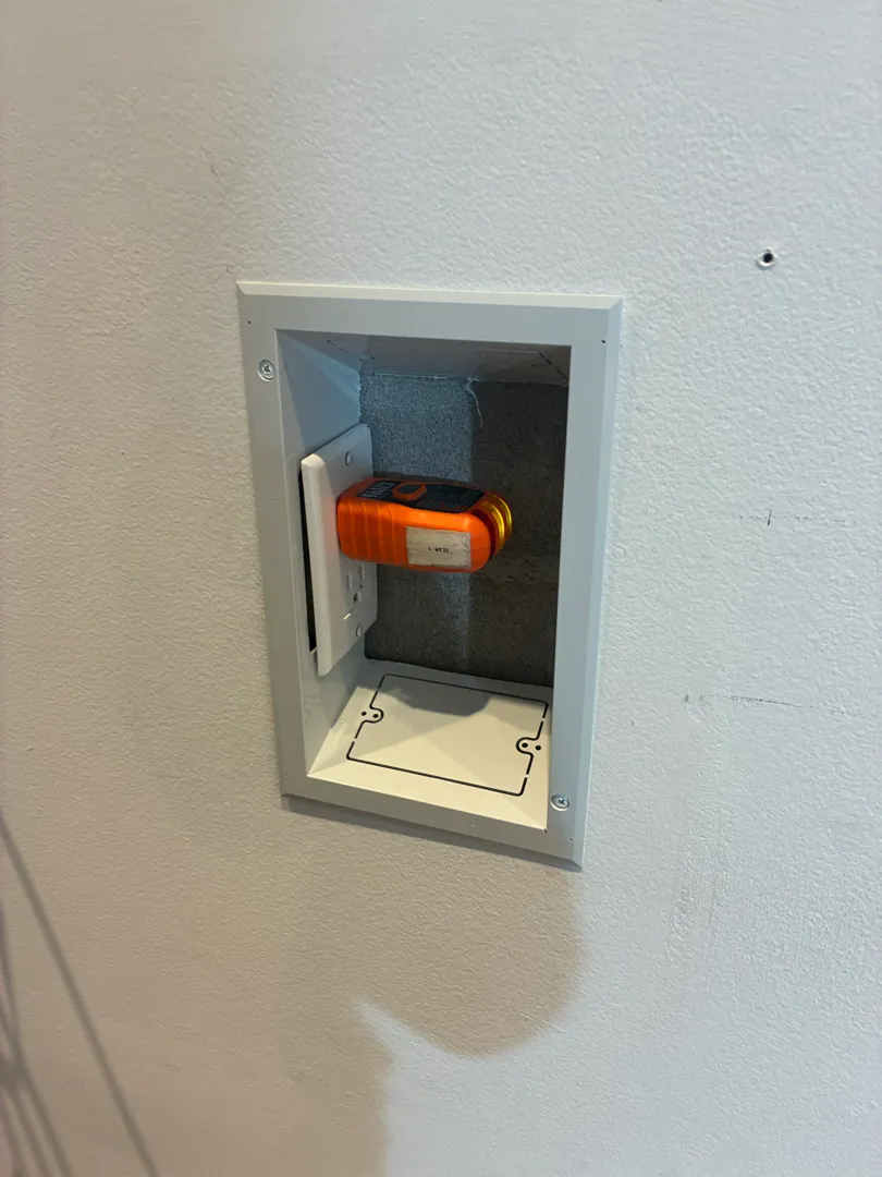 An orange tester sitting inside a recessed wall outlet box.