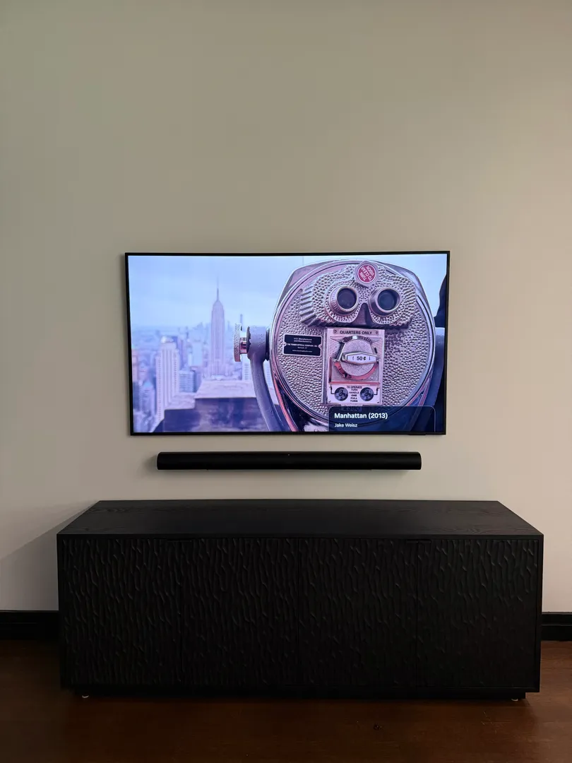 The mounted TV showing a city skyline image above the soundbar and black cabinet.