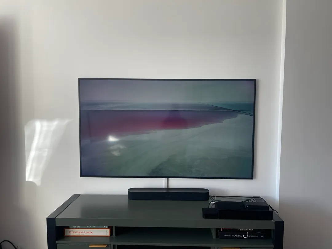 A slim Frame TV hanging flat on a white wall above a black soundbar on a green console.