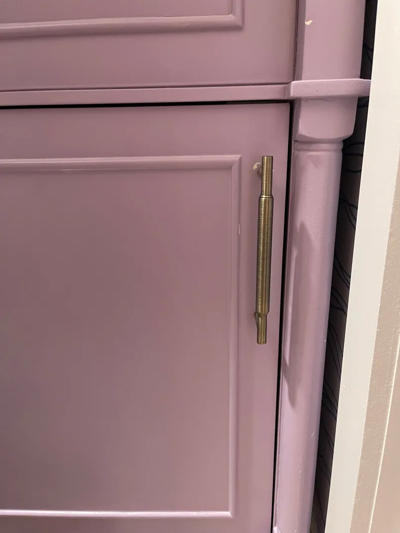 A brass cabinet pull mounted on a lavender cabinet door.