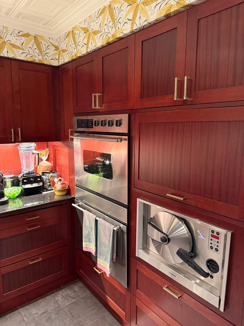 A kitchen corner with built-in wall ovens and a steam oven set into dark red cabinetry.