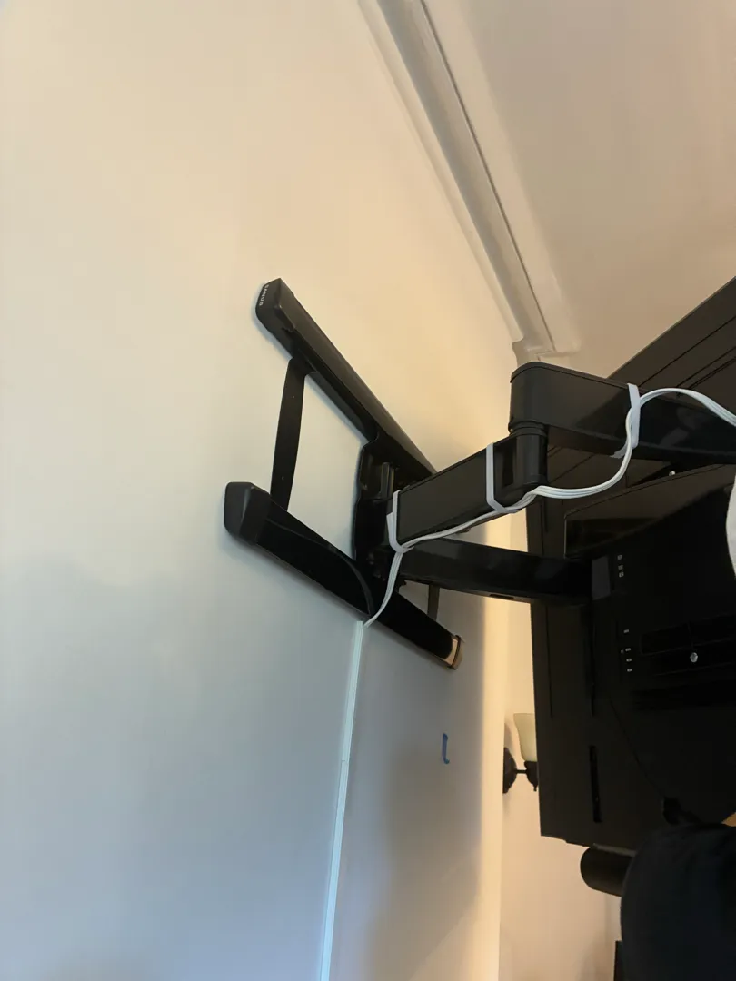 A black full-motion arm mount bolted above a fireplace with a TV hanging on its arms.