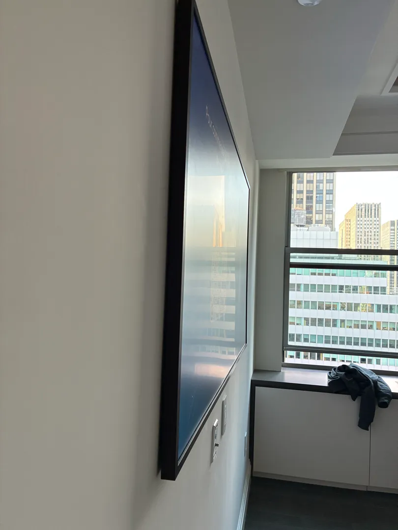 Side view of a black-framed TV sitting close to the wall with a window and city buildings beside it.