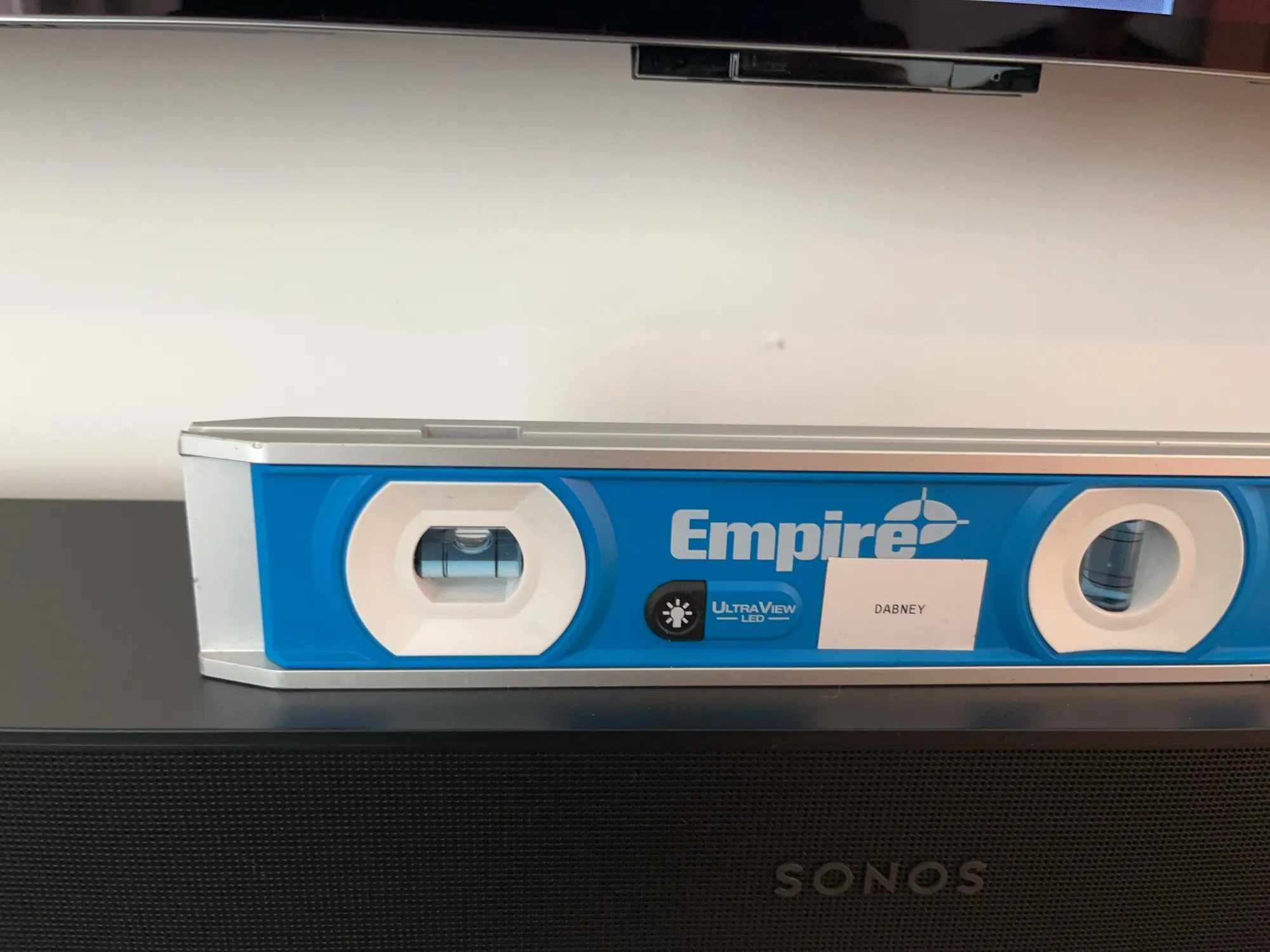 A level resting on the soundbar below a wall-mounted TV during an alignment check.