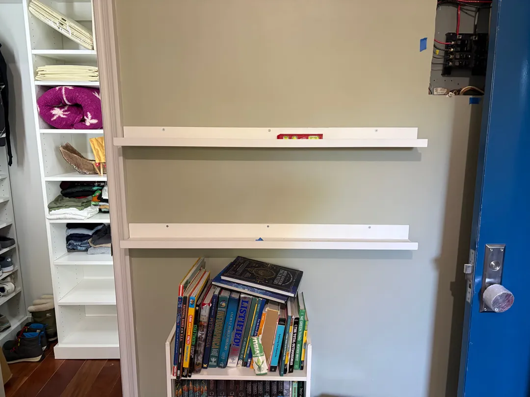 Two long floating shelves mounted above a bookshelf, next to an open closet.
