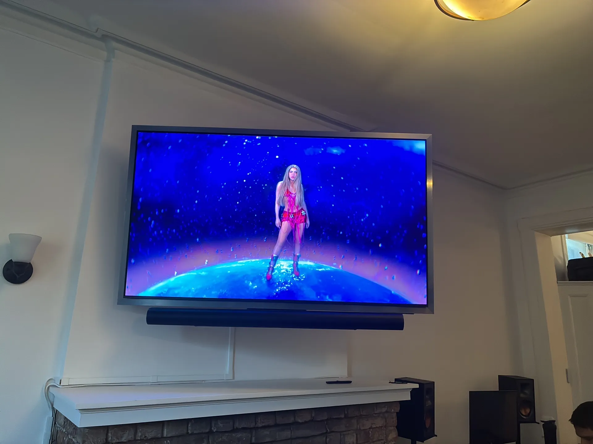 A wall-mounted TV with a soundbar below it, a cord cover and bookshelf speakers on the mantel.