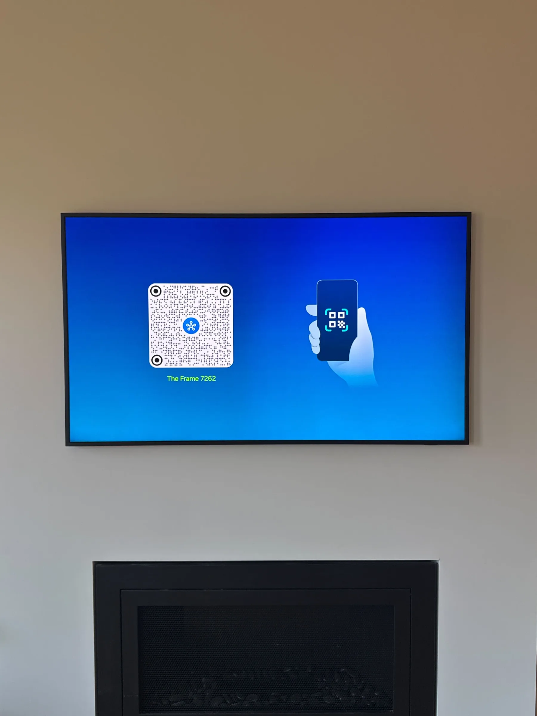 A Samsung Frame TV mounted above a fireplace, showing its setup screen with a QR code.