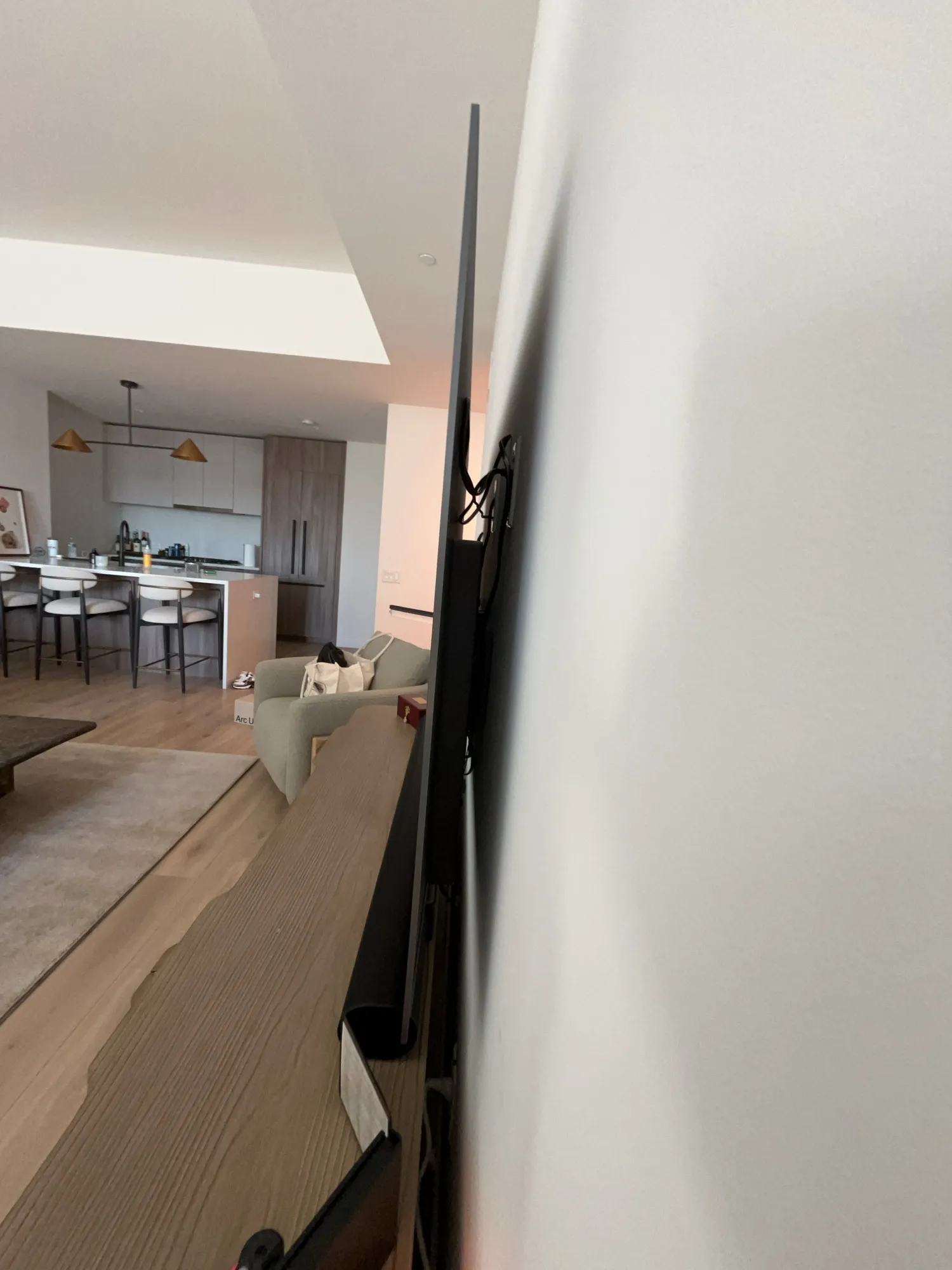 A hallway view of a TV mounted flush on the wall, with the kitchen in the background.