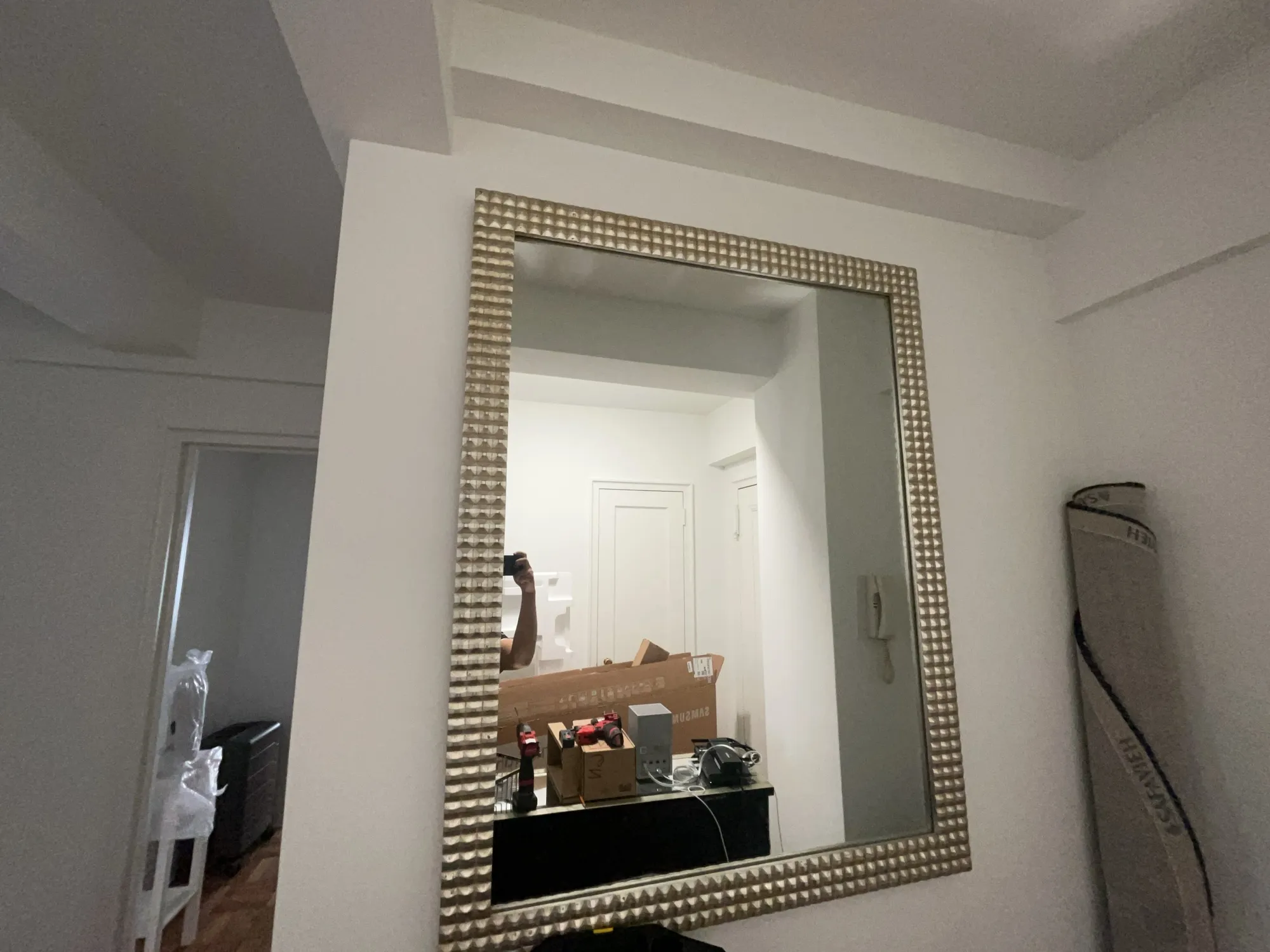 A large framed mirror on a wall, with tools and boxes reflected in it.