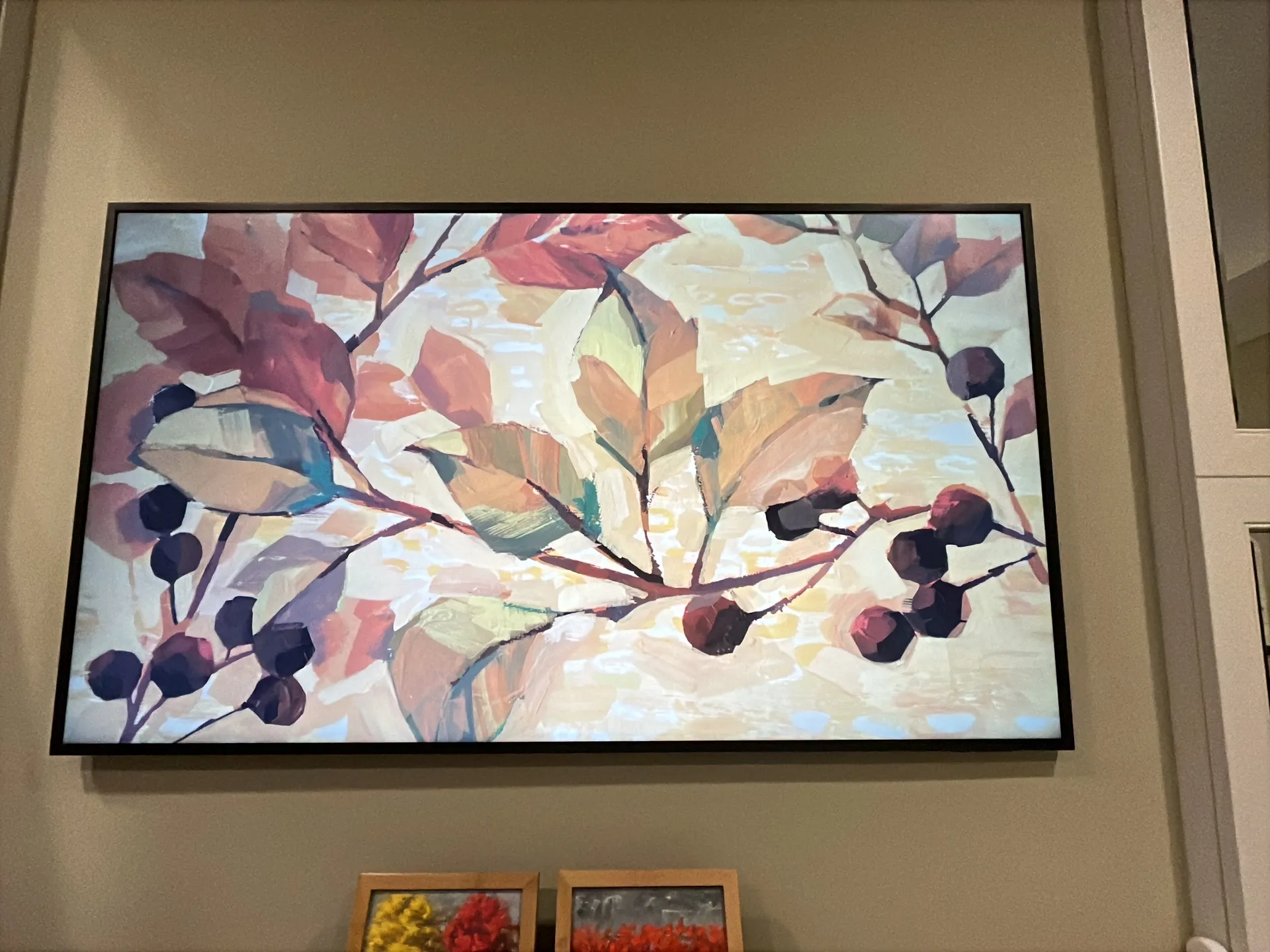 A Frame TV in art mode displays a floral painting, mounted above a stone ledge holding two small framed paintings.
